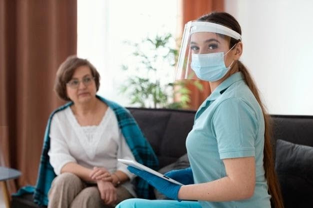 Nurse wearing a face shield assisting an elderly woman with in-home respiratory treatment