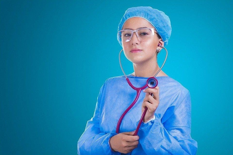 Doctor in medical scrubs and cap holding a stethoscope against a blue background, representing respiratory health care and nebulizer use.