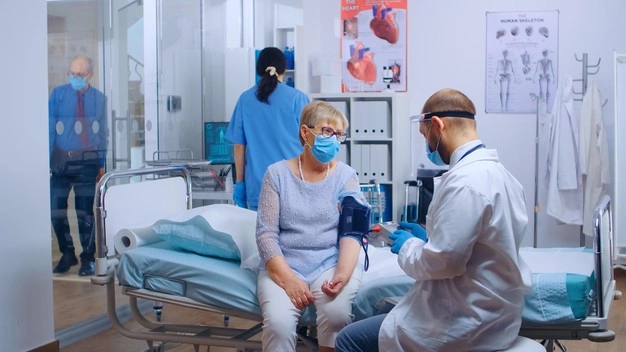 Doctor consulting with a patient in a hospital room while wearing masks and medical scrubs