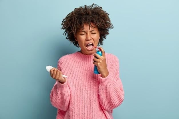 Woman in a pink sweater using an inhaler, representing difficulty breathing or bronchitis symptoms.