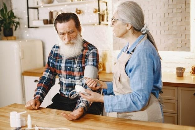 Older woman assisting a man in checking his blood pressure at home in the kitchen
