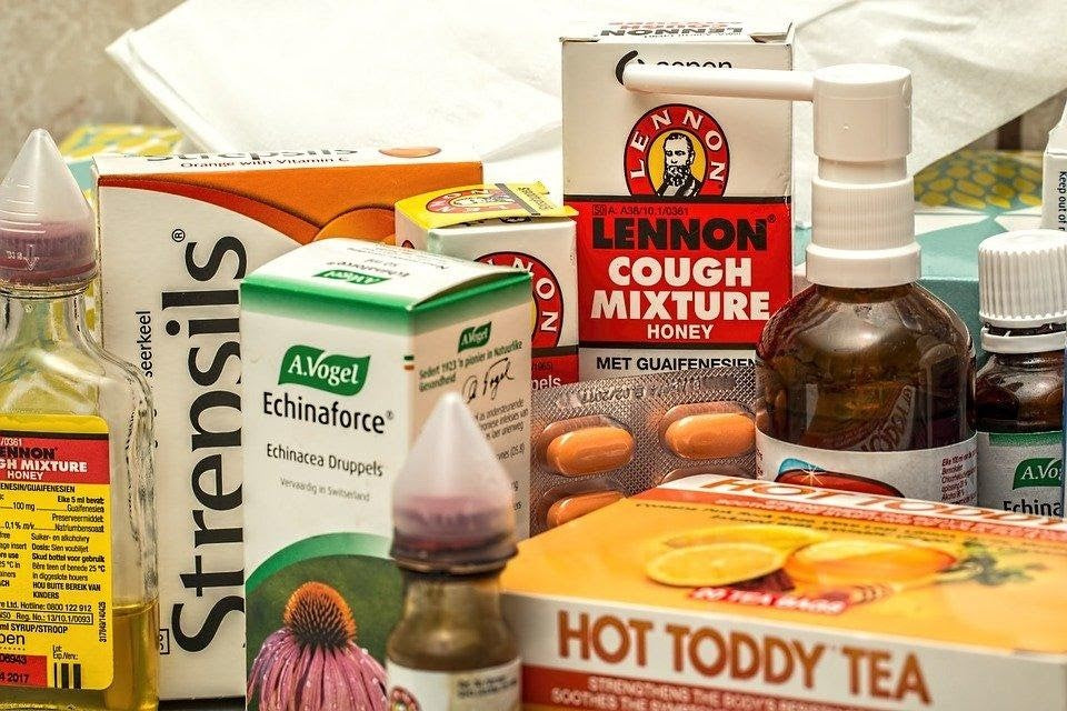 Home remedies and over-the-counter treatments for pneumonia, including cough syrup, throat lozenges, hot toddy tea, and vitamins on a table