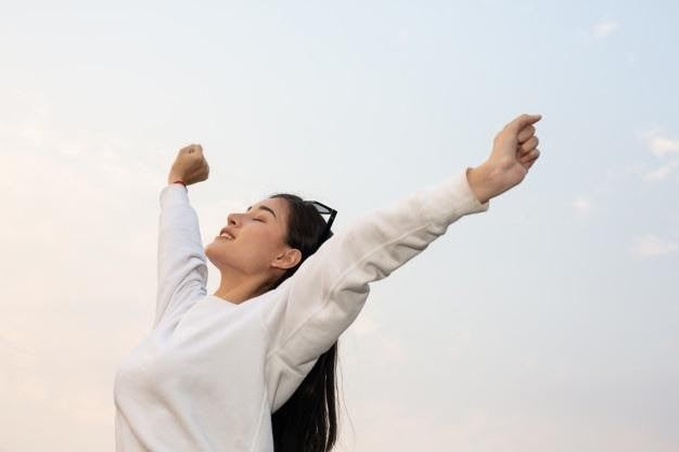 Woman outdoors with arms raised, breathing deeply and enjoying fresh air