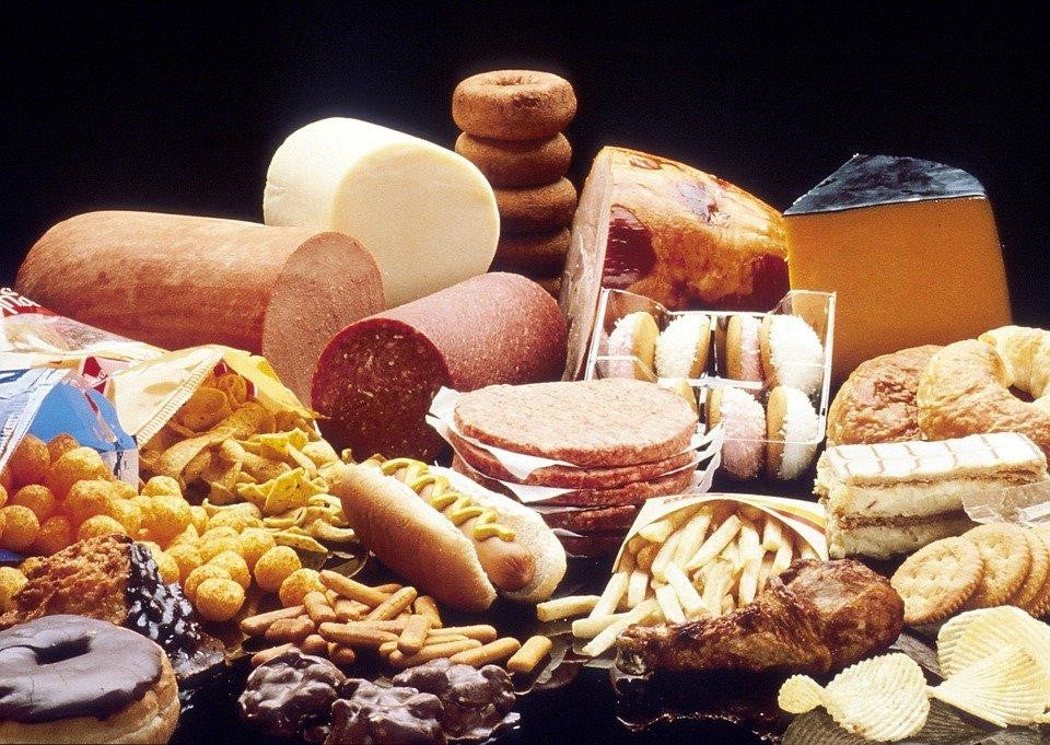 Assorted high-cholesterol foods including bread, cheese, sausage, and pastries arranged on a table