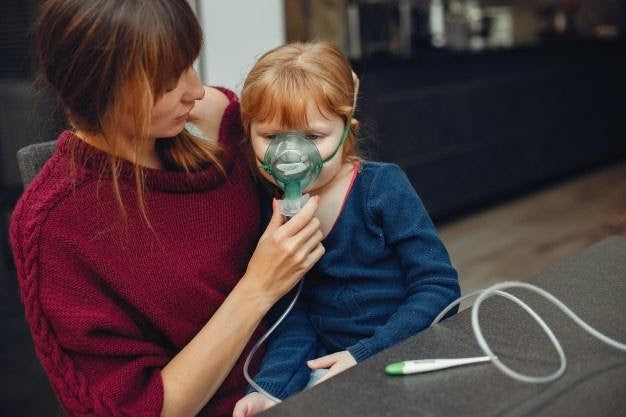 Mother helping young child use a nebulizer with an oxygen mask for respiratory treatment