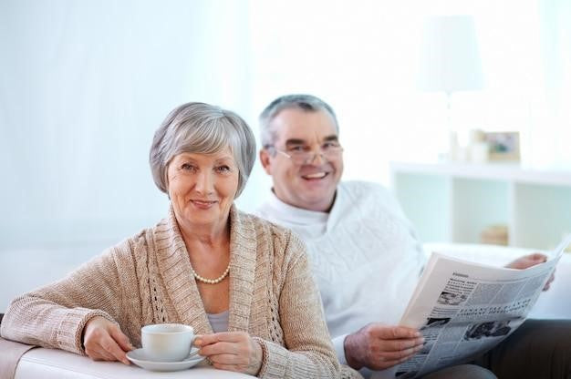 Smiling senior couple sitting together with coffee and newspaper, representing comfort and wellness while managing COPD