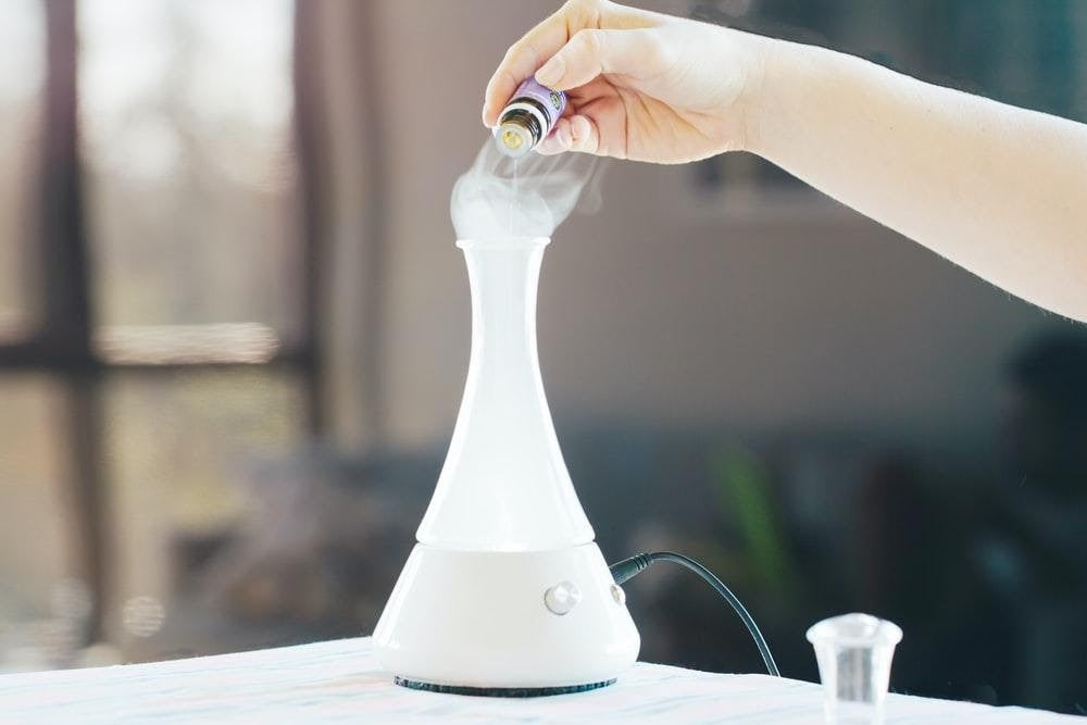 Hand placing medication into a white portable nebulizer on a table for respiratory treatment at home.         Ask ChatGPT