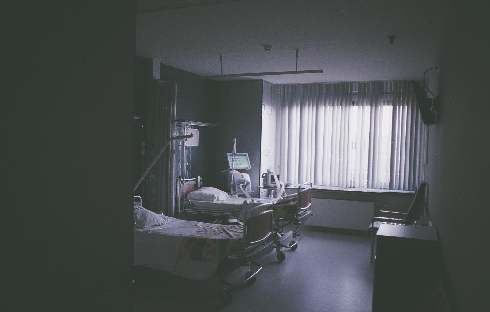Empty hospital room with bed and medical equipment lit by window, representing stroke and hypertension-related hospitalization.
