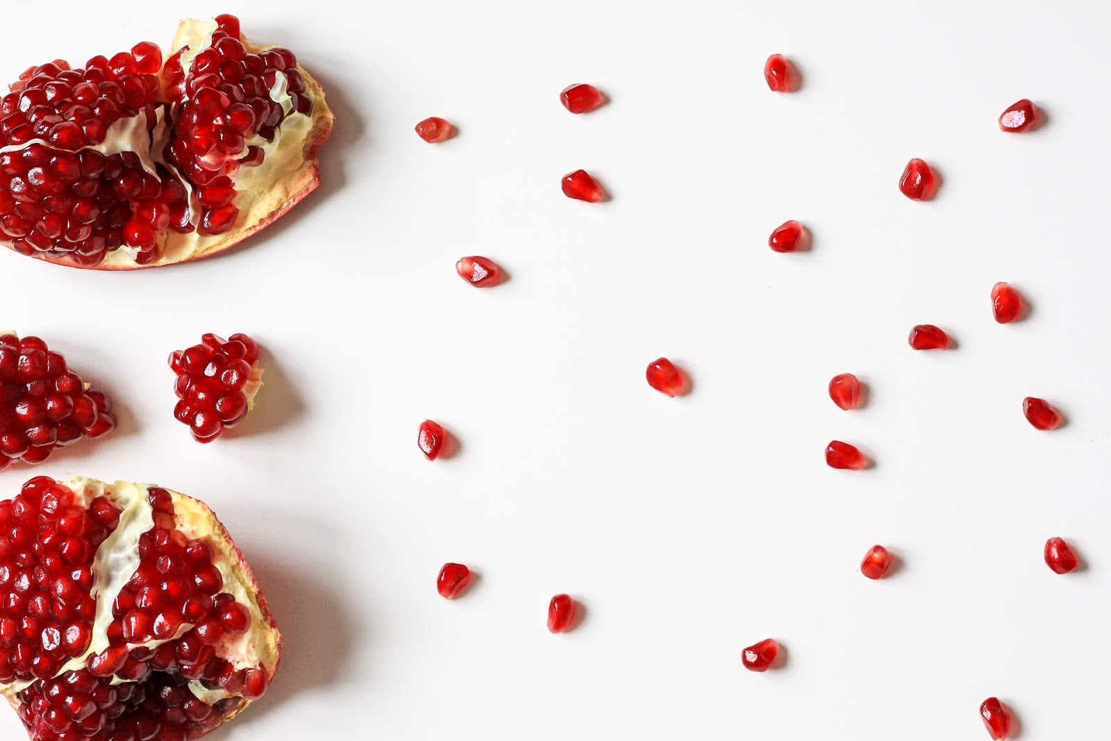 Slices of pomegranate with scattered seeds on white background, a heart-healthy fruit known to support lower blood pressure.