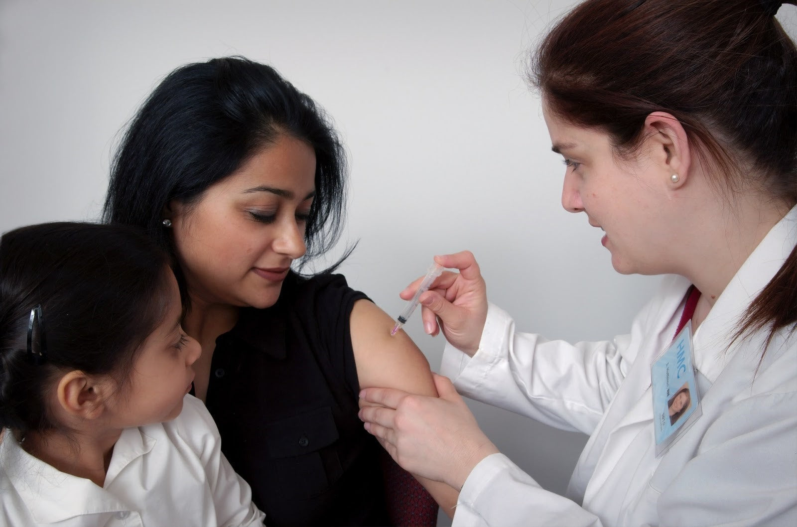 Female doctor giving a vaccine to a smiling woman, with a child watching closely — representing preventive healthcare and respiratory infection protection