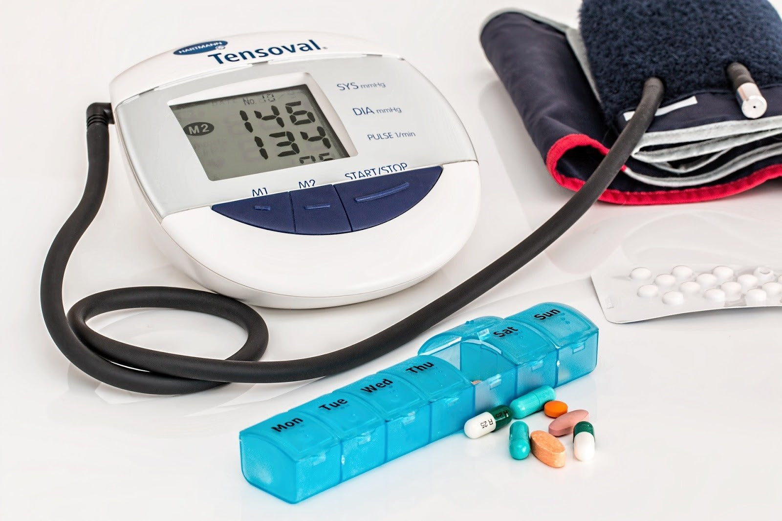 Blood pressure monitor, pill organizer, and hearing aid on a table – tools used to manage cognitive and cardiovascular health