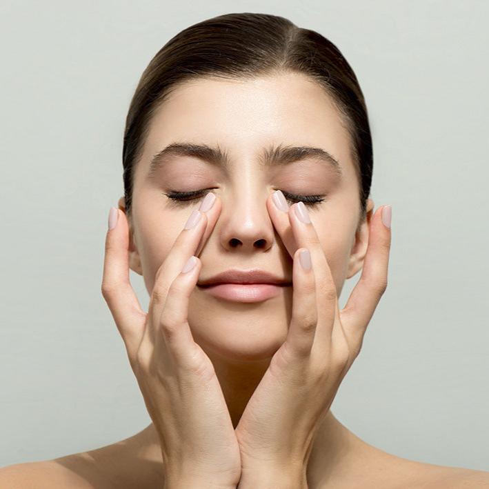 Woman gently massaging her eyes for dry eye relief and relaxation on neutral background
